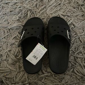 New with tags croc slides.  Never worn.  Includes croc charms